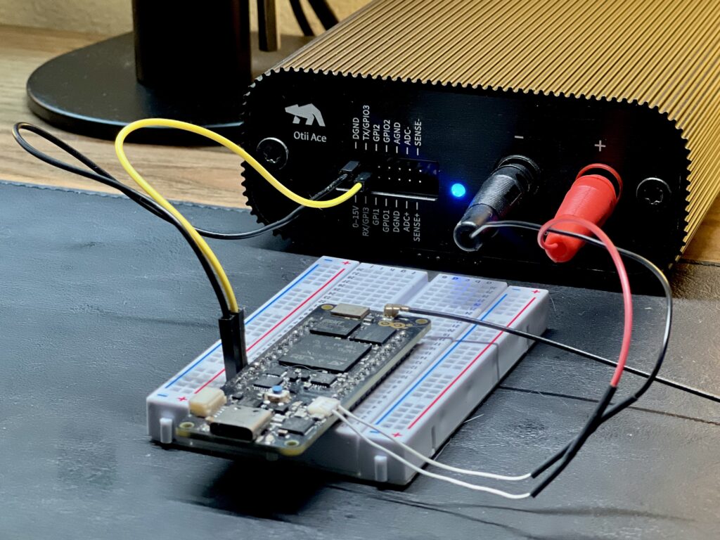 The image shows an Arduino Portenta H7 connected to an Otii Ace Pro via a breadboard. The Otii Ace Pro is supplying power and measuring the current of the Arduino device. The red and black banana plug wires are connected to the Otii Ace Pro’s positive and negative terminals, respectively, with the red wire attached to the positive power input of the Arduino and the black wire attached to its ground. Additional yellow and black wires connect the GPIO pins from the Otii Ace Pro to the Arduino for logging and data communication. The setup is actively powered, as indicated by the blue LED on the Otii Ace Pro.